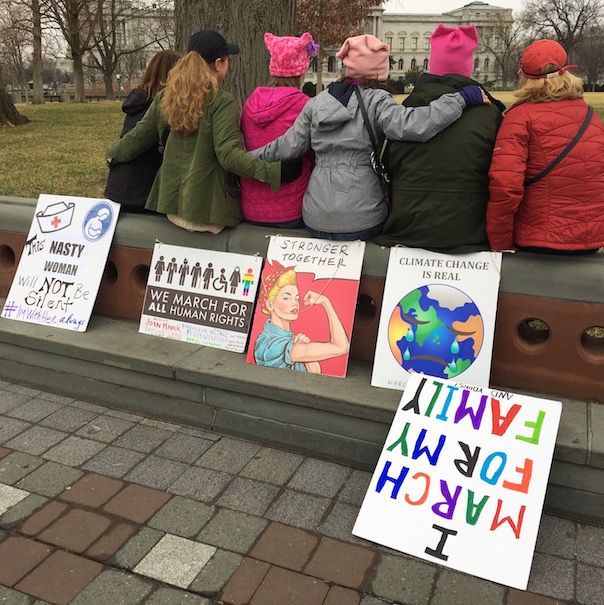 Women sitting on a wall with their signs at the Womens March on Washington DC, Jan 21, 2017